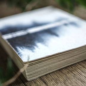 A6 målarbok, Skyddsruna, fotograferad utomhus i naturligt ljus. Mjuk fokus visar runmotiv och skogsmotiv.