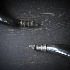 Detaljbild av mässingbandring på hornmuggen, visar metallhandverkets precision och naturlig hornstruktur