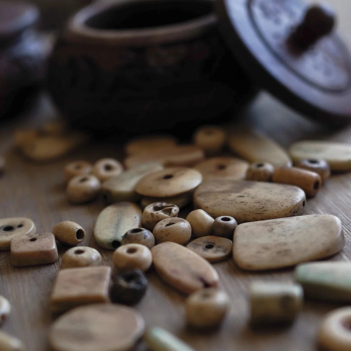 Blandning av vita benpärlor på trä. Pärlorna visar naturlig benåldrande med varierad färgtoning från cremevit till mörkare exponerad benyta. Formerna inkluderar rör, cylindrar, sfärer och rektangulära rummares.