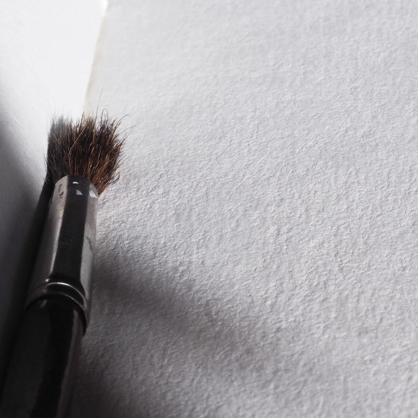 Närbild av målarpensel på texturerat vitt papper, visar fina fibrer i återvunnen bomullspapper