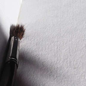 Närbild av målarpensel på texturerat vitt papper, visar fina fibrer i återvunnen bomullspapper