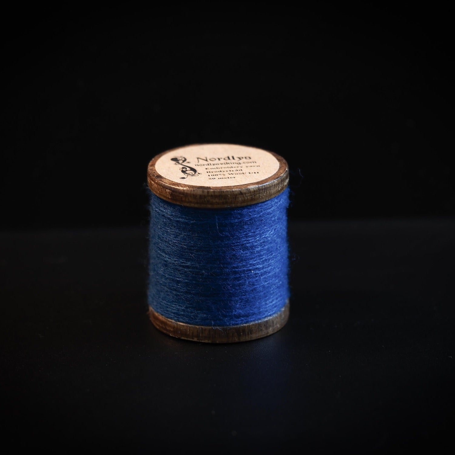 Blå broderitråd på trætromler med Nordlys-mærkning. Klassisk træspole med håndlavet look for vikingeinspireret broderi og håndværk.