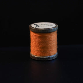 Brændt orange broderitråd på traditionelle trætromler med Nordlys-mærkning. Naturlig jordfarvet tone inspireret af historiske vikingetekstilfarver.