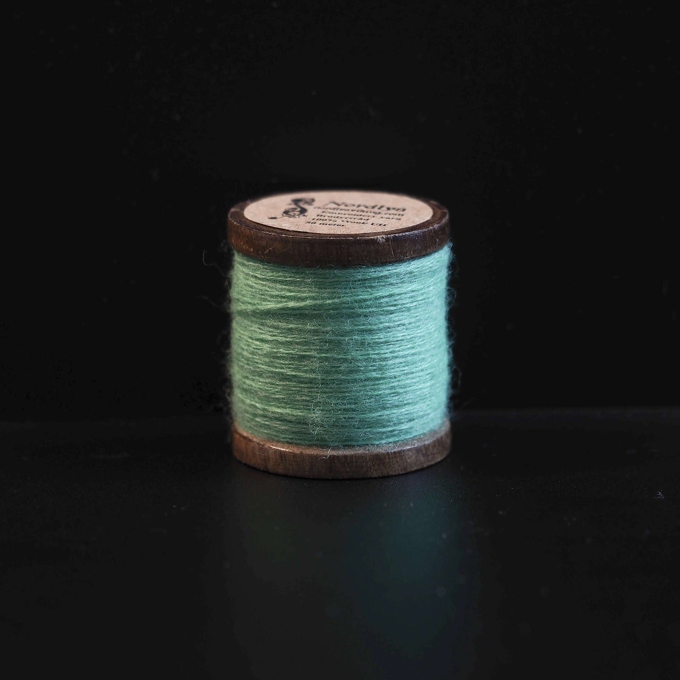Sort broderitråd på trætromler med Nordlys-logo. Klassisk farve til traditionel vikingeinspireret broderi og formel skandinavisk tekstilkunst.