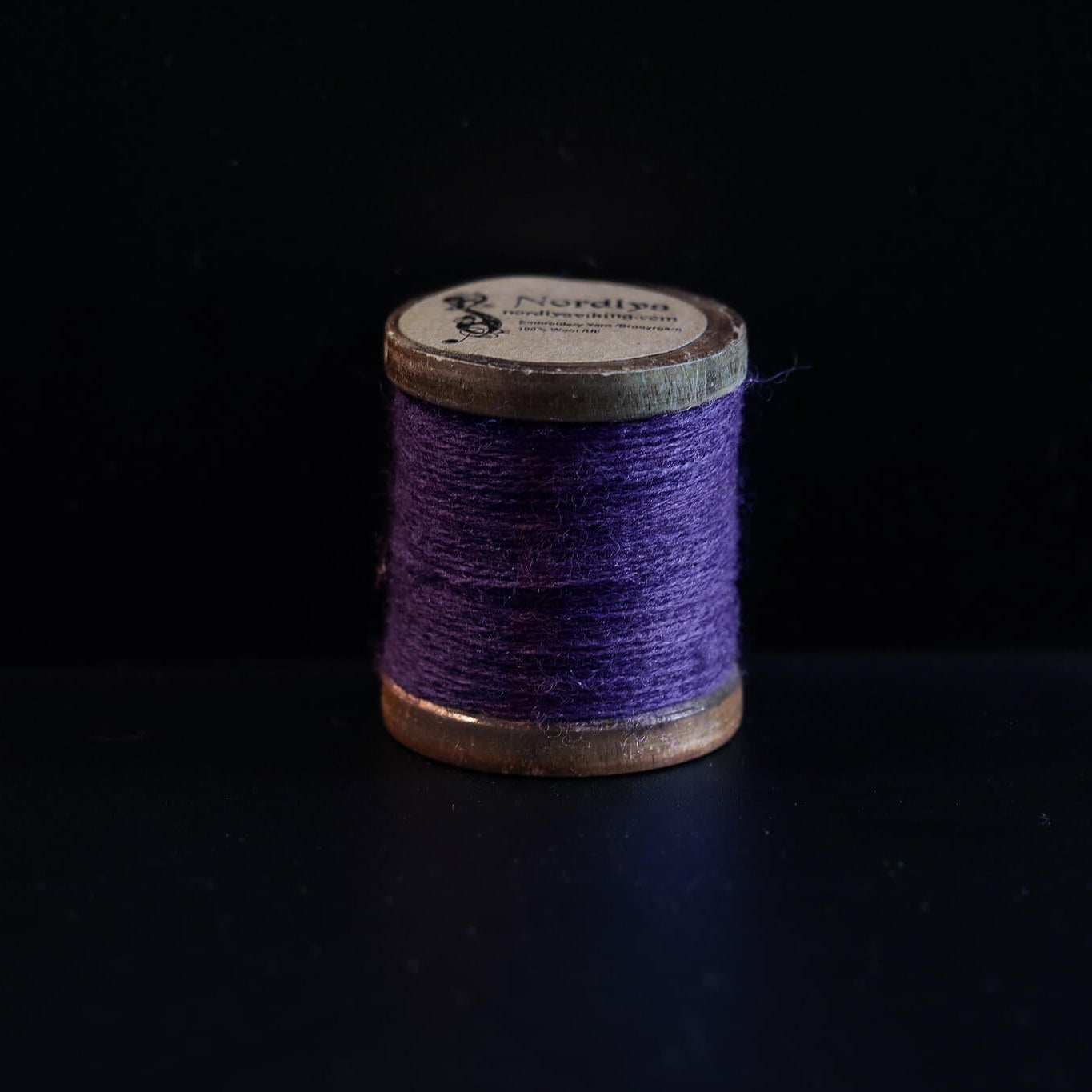 Lilla broderitråd på trætromler med Nordlys-mærkning. Dyb lilla farve perfekt til traditionelt vikingebroderi og tekstiler.