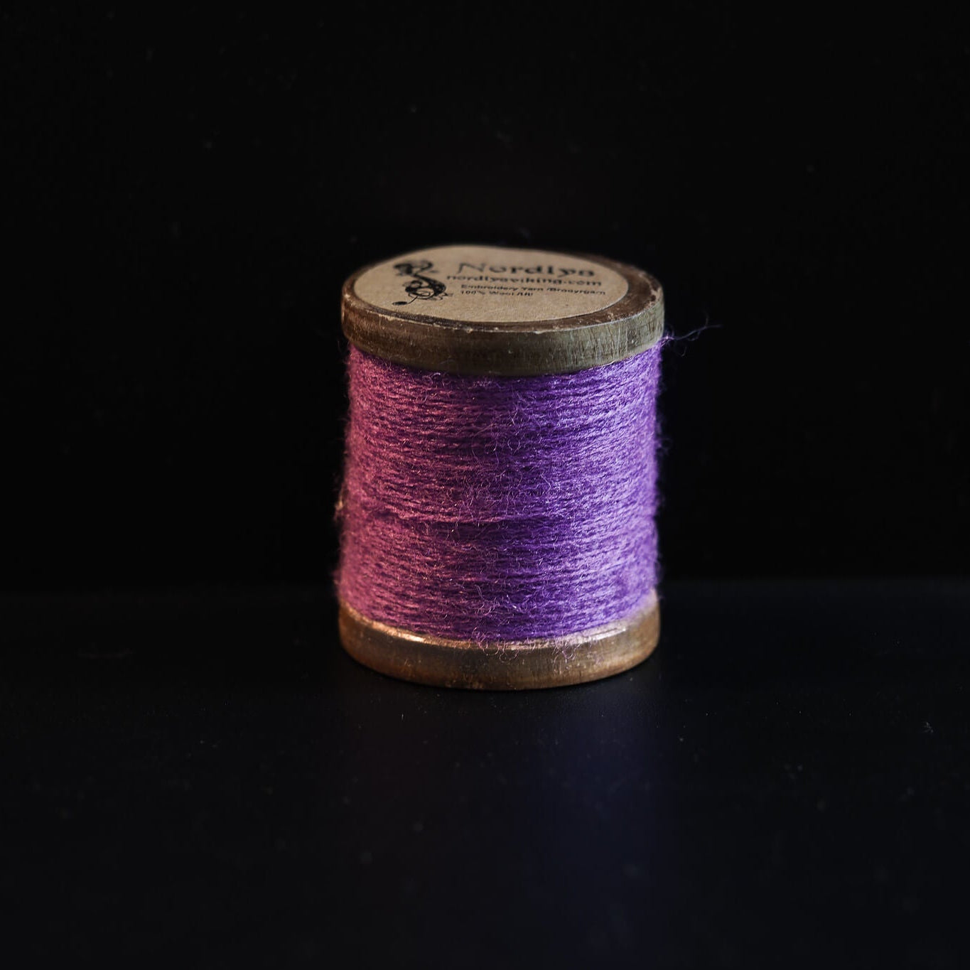 Lyserød-lilla broderitråd på trætromler med Nordlys-mærkning. Blød farvetone egnet til detaljeret vikinge-inspireret broderi og traditionelt håndværk.