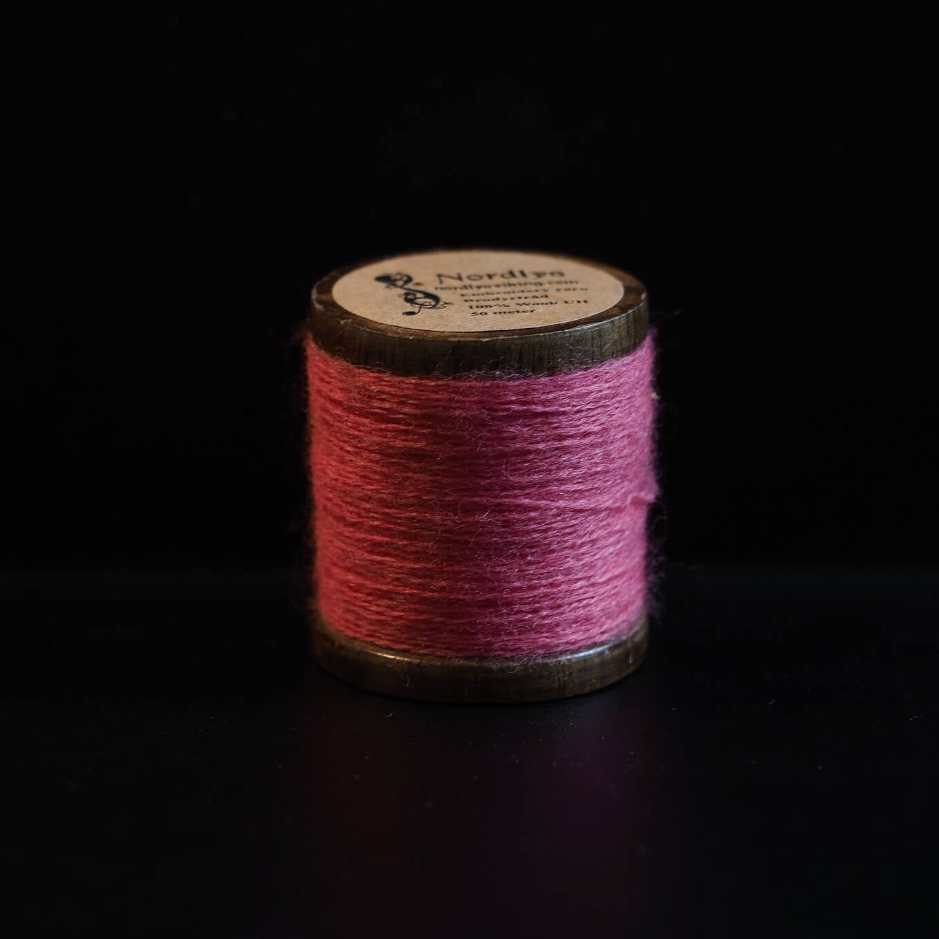 Rød broderitråd på traditionelle trætromler med Nordlys-mærkning. Dyb rød farve inspireret af vikingedragter og traditionelt skandinavisk broderi.