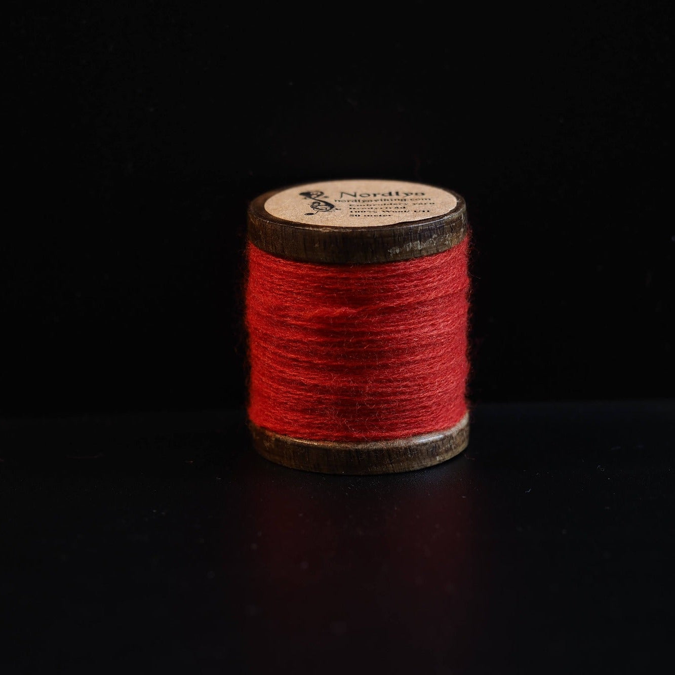 Lys rød broderitråd på trætromler med Nordlys-logo. Klassisk farve til vikingeinspireret broderi og traditionel skandinavisk tekstilkunst.