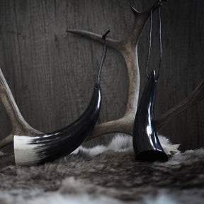 Litet horn med läderband, hängande på person i bruna byxor. Handgjort från ko med naturlig kornstruktur och lackerad mörk insida.