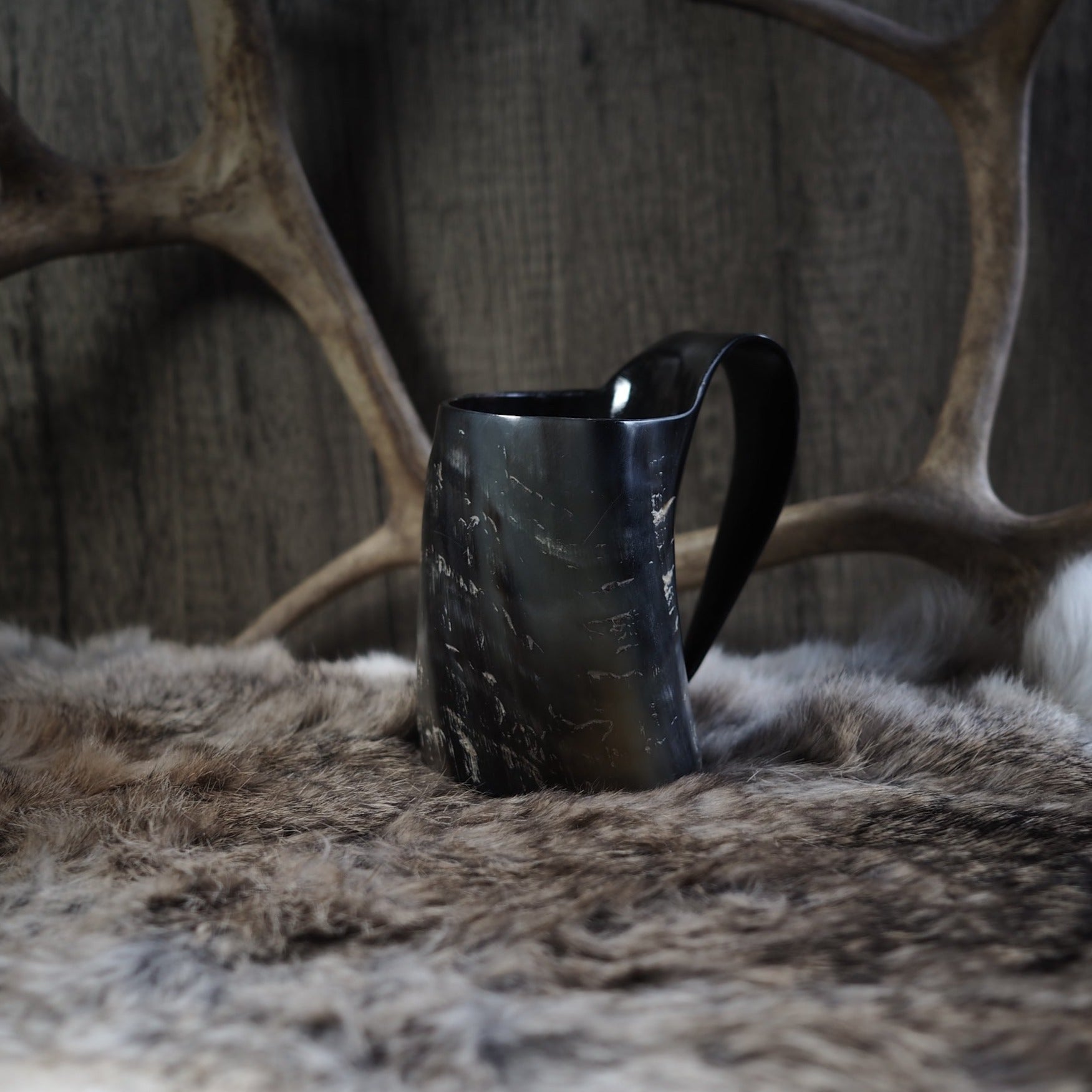 Mörk hornmugg på djurhud framför rustik vägg. Detaljbild som visar hornets naturliga struktur, ådring och åldrad patina.