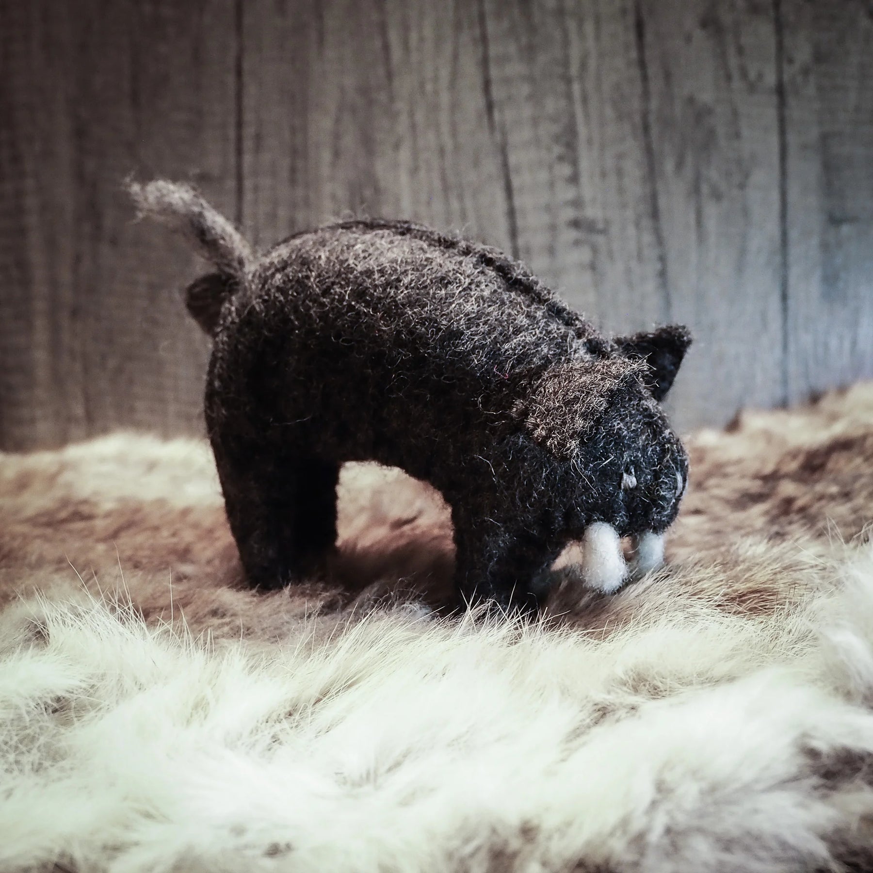 Handgjord filtad gris i grått ull. Figuren står i framåtlutad ställning med frambenens utsträckta. Detaljerad utförning visar öron, nos och lätt krullad svans. Tillverkad av 100% ull och färgad med vattenbaserade färger i Nepal. Naturlig texturd wollytersättning är synlig.