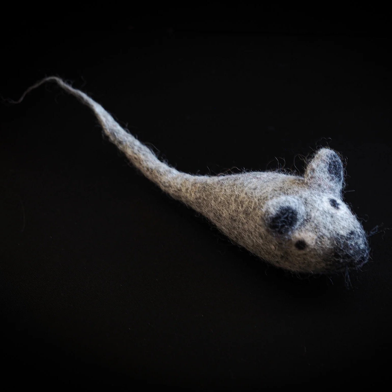 Handfelted wool mouse in natural tan-grey shown from above angle, displaying rounded body and curved tail