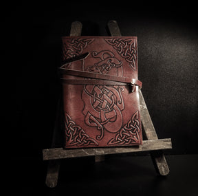 Person wearing leather Viking dragon notebook accessory with embossed knotwork patterns in moody dramatic lighting