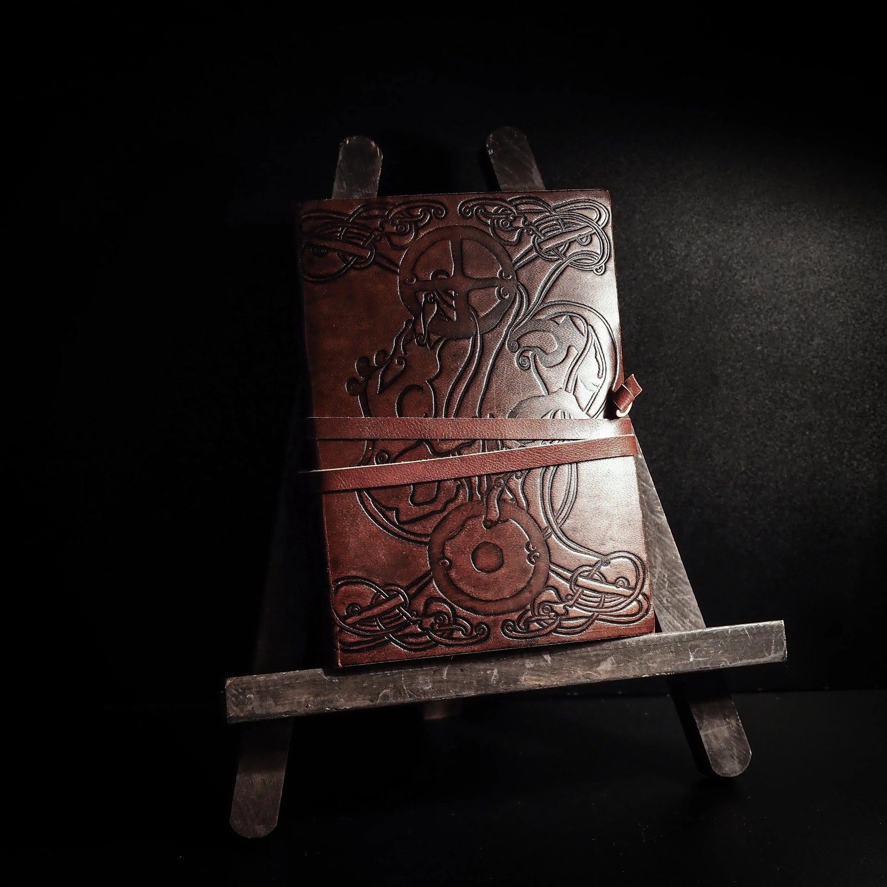 Läderbunden anteckningsbok med präglat vargmotiv och keltiska knutar, ståendes på träställ