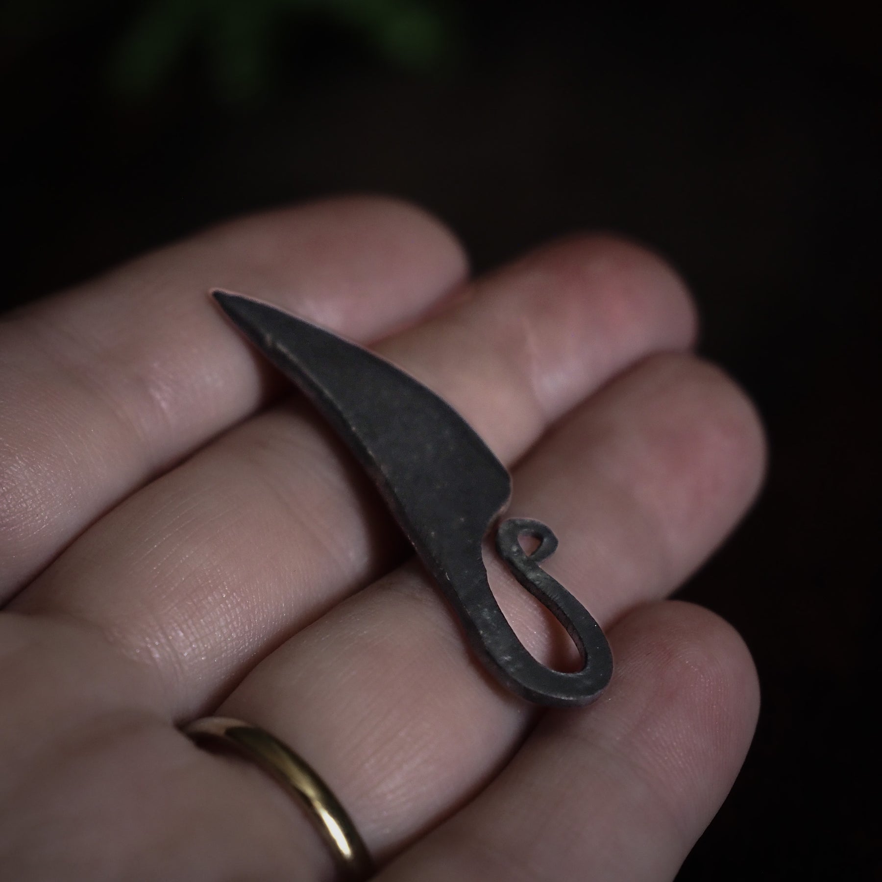 Kvinnokniv mini håller i hand. Detaljbild som visar skalan och smidkaraktären på den lilla mörka metallklingen med krökande form och ögla för snöre.