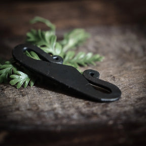 Närbild av svart järnpendant med spiralformad snyggla på rustik träyta med granbarr