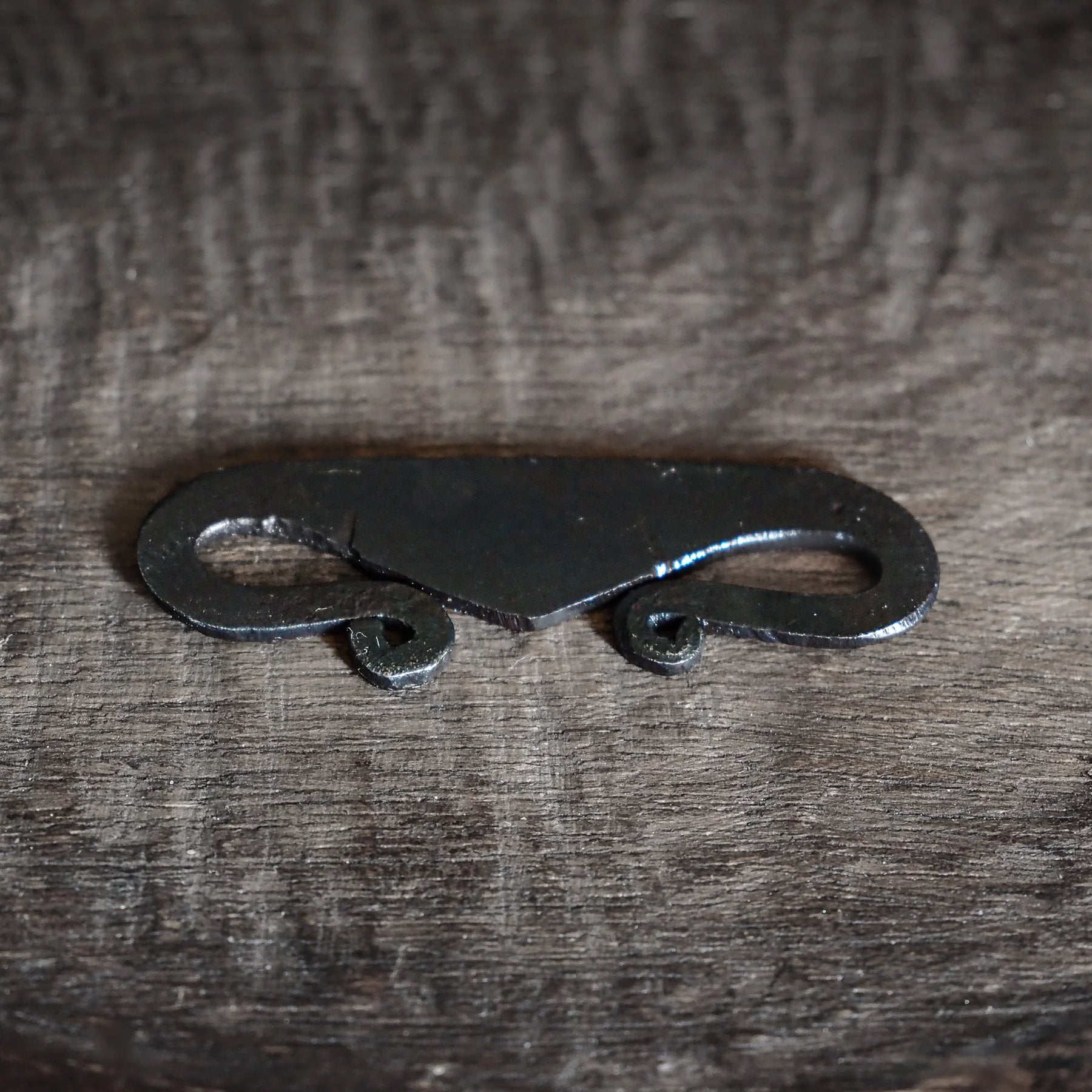 Viking-inspirerad brosch av järn med S-kurva och ögla-ändar, fotograferad på textilbakgrund