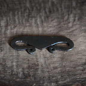 Viking-inspirerad brosch av järn med S-kurva och ögla-ändar, fotograferad på textilbakgrund