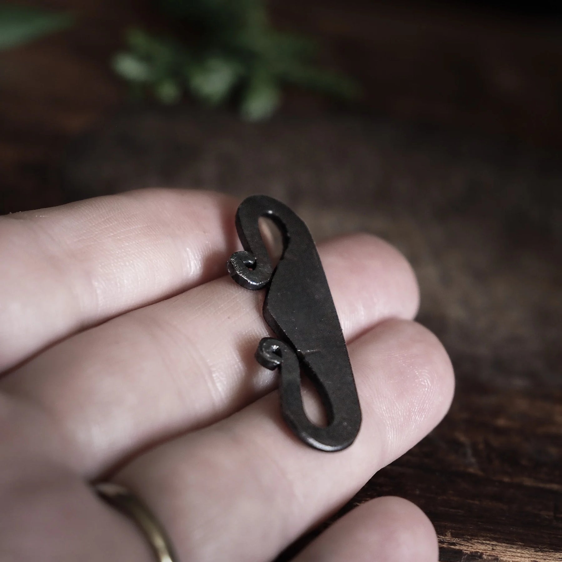 Järnpendant hållen i hand mot skogsbackgrund, visar spiraldetaljer och autentisk oxiderad finish