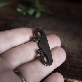 Järnpendant hållen i hand mot skogsbackgrund, visar spiraldetaljer och autentisk oxiderad finish