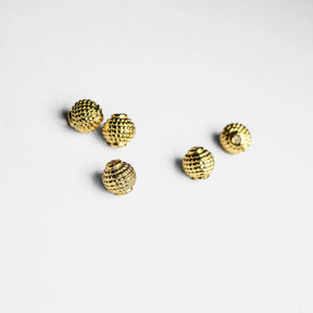 Fem guldfärgade metallpärlor med granulerat rutmönster på vit bakgrund