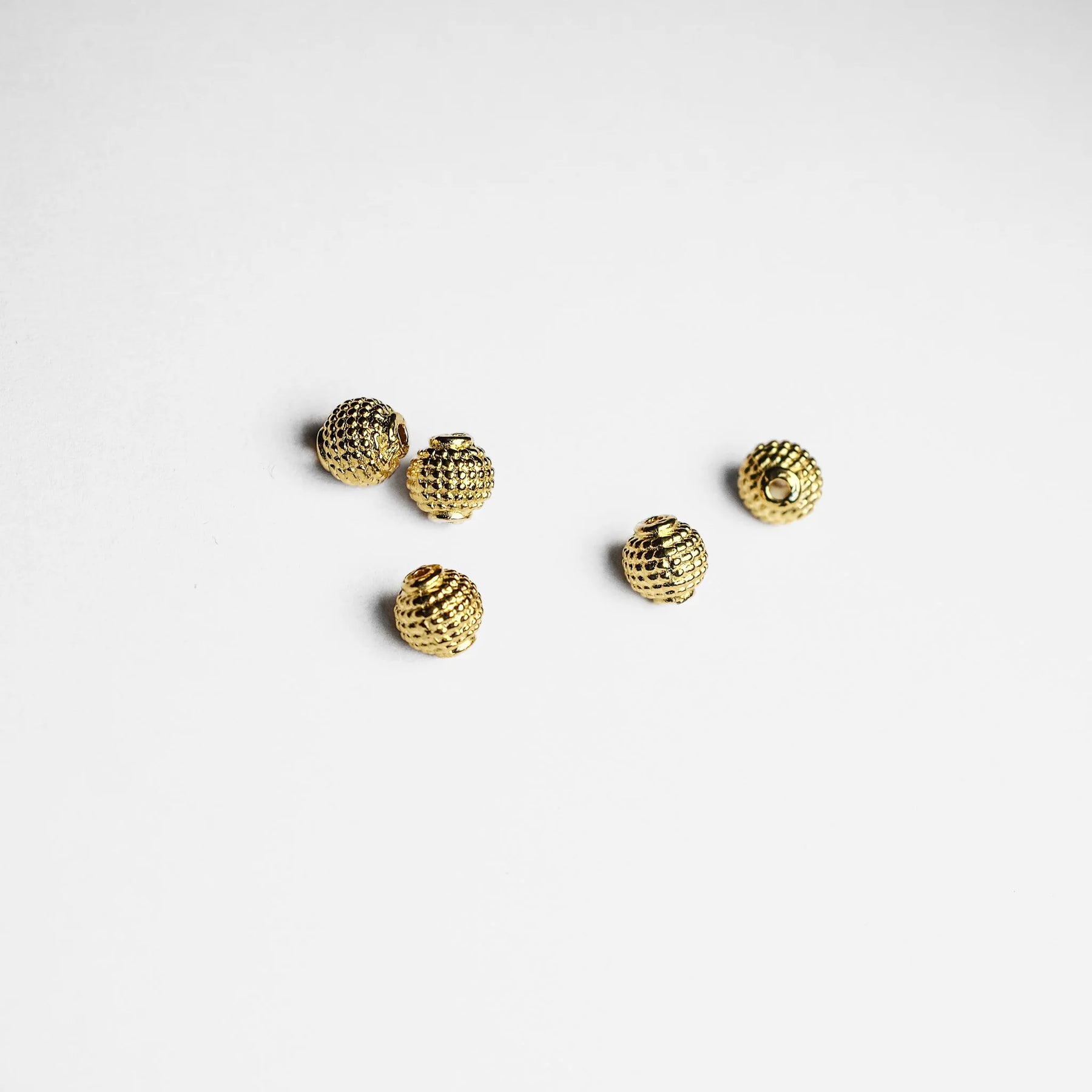 Fem guldfärgade pärlor med rutmönstrad granulering på ljus bakgrund, ovanifrånvy