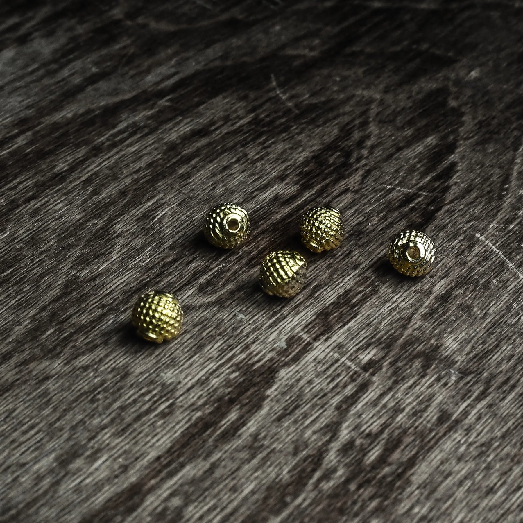 Fem guldfärgade Freja-pärlor med dekorerad yta på mörkt träunderlag, låg vinkel