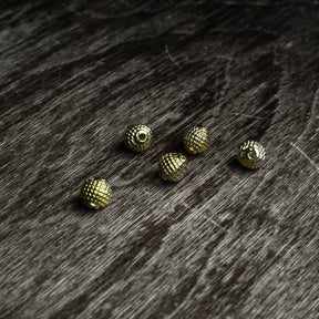 Fem guldfärgade Freja-pärlor med dekorerad yta på mörkt träunderlag, låg vinkel