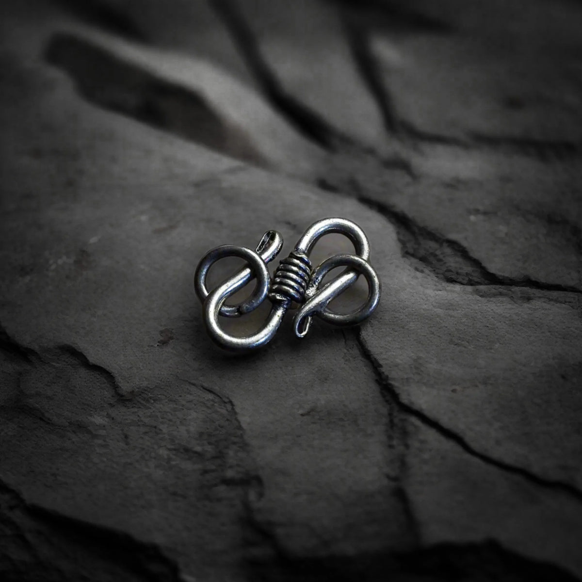 Slutskänkla av silver: två motsatta öglor förbundna med en dekorativ knut i mitten. Makrofoto på grå sten, visar mekanismen i detalj.