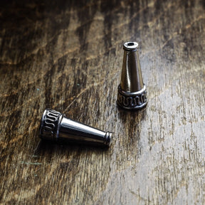 Två silverpläterade ytterpärlor med konisk form på träyta. Visar detaljerad dekorativ ring och mässingsarbete vid basen av varje pärla.