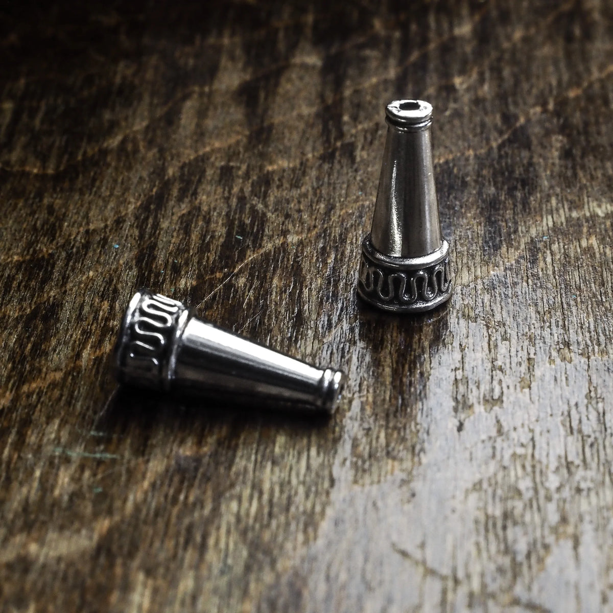 En silverpläterad ytterpärla med konisk form och dekorativ texturerad ring vid basen. Fotografi på rustik träyta som visar pärlans 22mm längd och hålöppning.