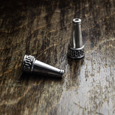 En silverpläterad ytterpärla med konisk form och dekorativ texturerad ring vid basen. Fotografi på rustik träyta som visar pärlans 22mm längd och hålöppning.