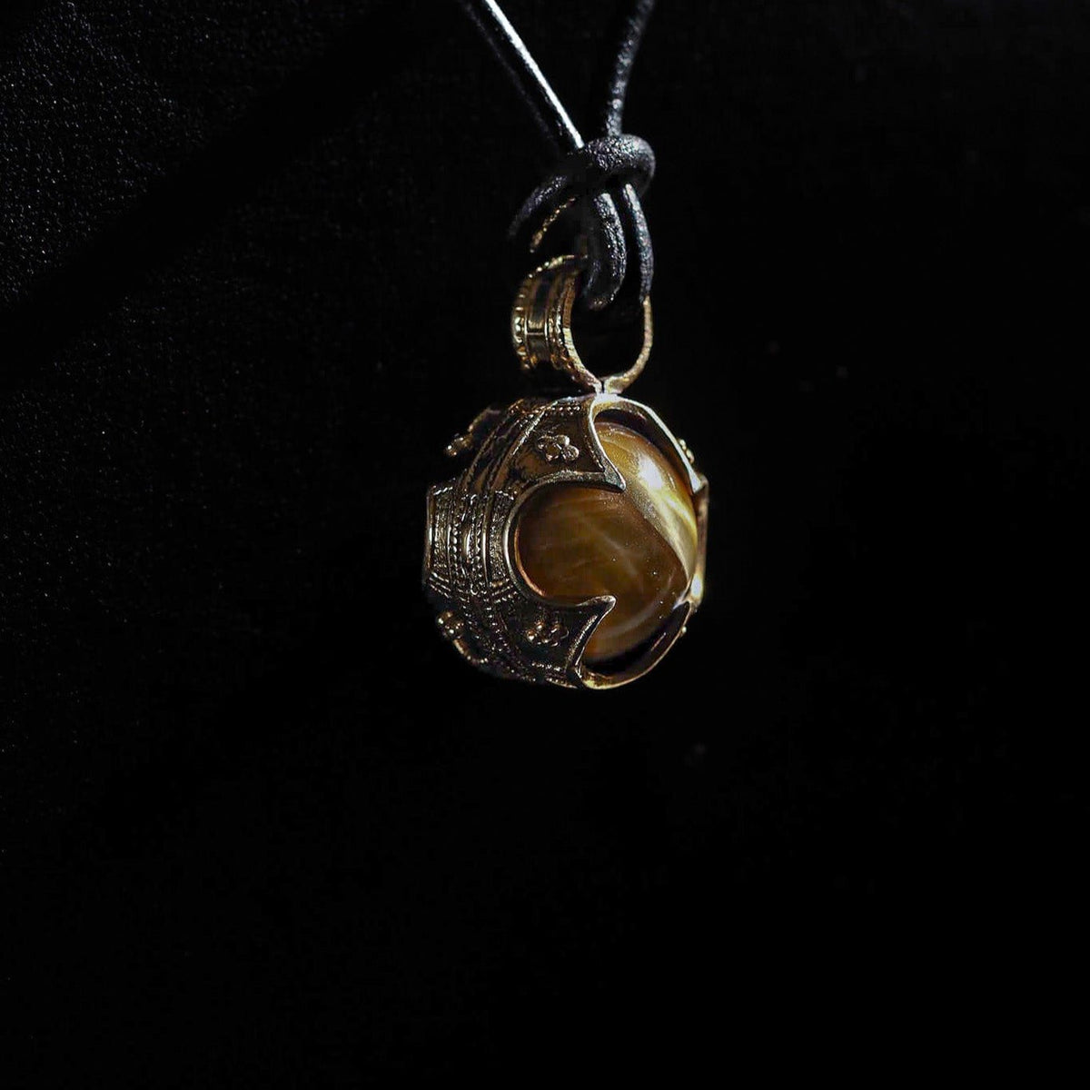 Silverpläterad gotlandshänge med tigeröga på svart snöre. Tigeroögestan med varmt guld-brunt ljusspel är infattad i en dekorativ silversmontering med vikingisk tvinnad kantdesign.