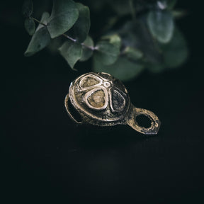 Mässingklocka med 30mm diameter och dekorativ prickad yta på mörk bakgrund, hängande från ögla. Närbildsfotografi som visar metalglans och texturerad design.