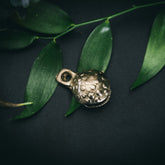 Mässingklocka i närbild med tydlig prickad och groplad yta. Små cirkulära reliefmönster täcker hela ytan. Snöre genom ögla synligt. Naturlig belysning visar metallglans och hantverkskvalitet.