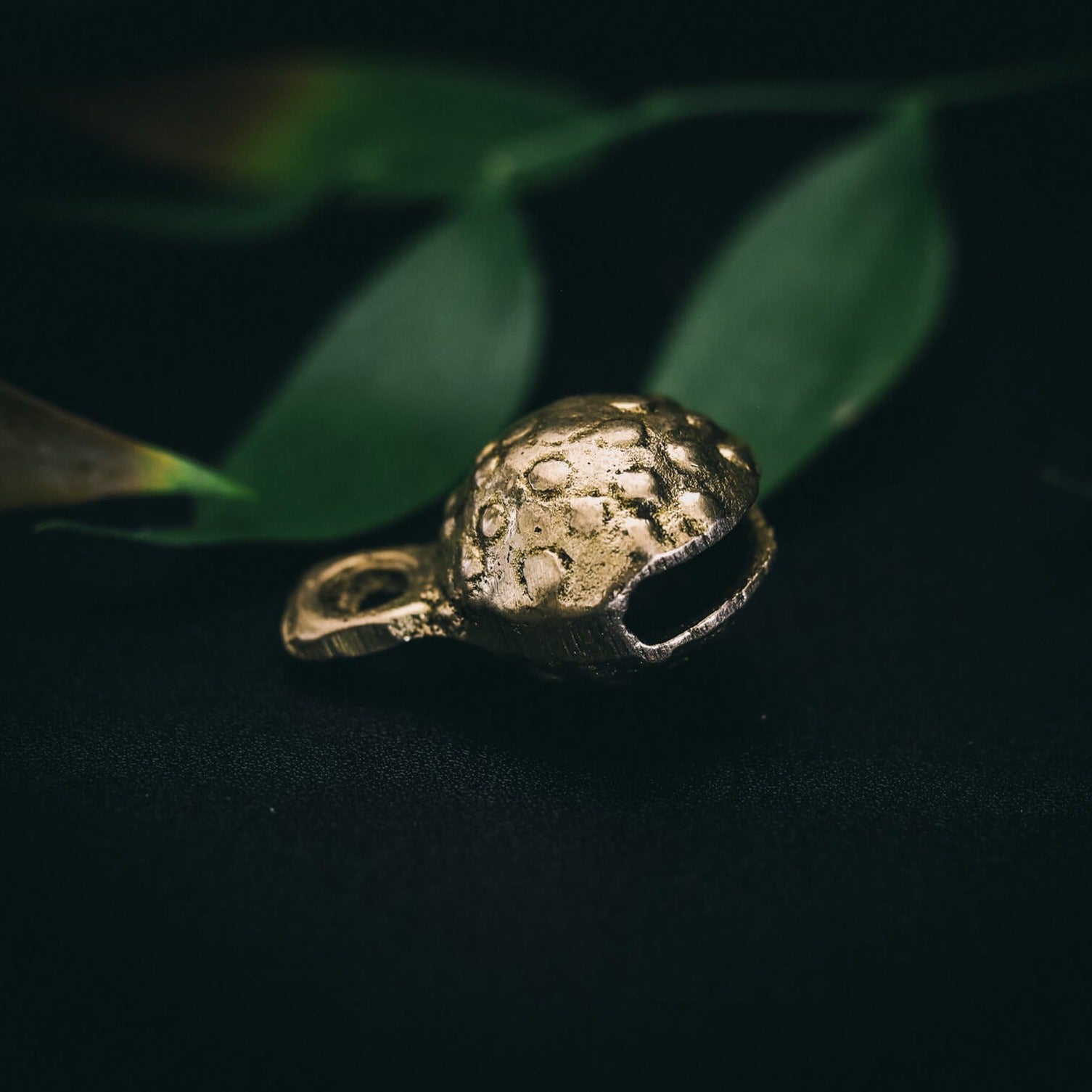 Närbild av mässingklocka med prominent prickad och groplad yta. Sfärisk form med regelbundet arrangerade cirkelformade reliefmönster. Grön naturlig bakgrund. Produktphotografi som visar detaljer.