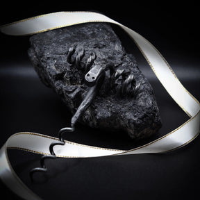 Bagge-skruv presenterad med silver/grå band med guldkant för lyx-packningseffekt. Ram-huvud visar detaljerat metallhantverk med synliga öga och horndetaljer. Dunkelstensunderlag understryker artisan-estetik. Kontrollerad belysning betonar både verktygets metallhantverk och presentationskvalitet. Tjänar både produktdokumentation och lyx-gåva-marknadsföring.