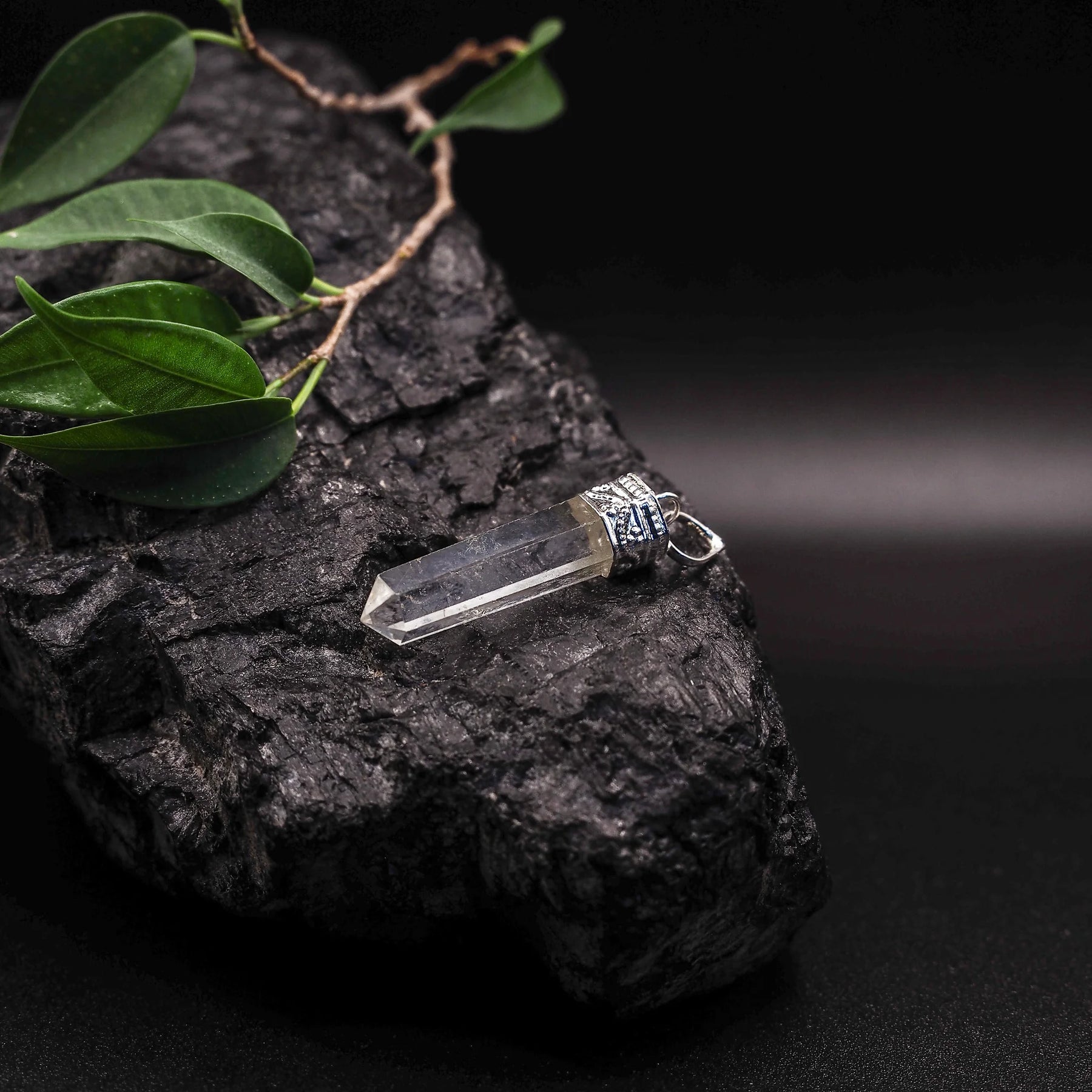 Bergkristallhänge med dubbelspetsad form och silverfärgat mässingsfäste, omgiven av gröna blad