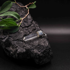 Bergkristallhänge med dubbelspetsad form och silverfärgat mässingsfäste, omgiven av gröna blad