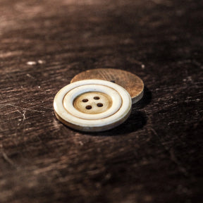 Stor benknapp från handsvarvning med naturlig benfargatonad och synliga drejarmarkeringar, fyra håll för tråd