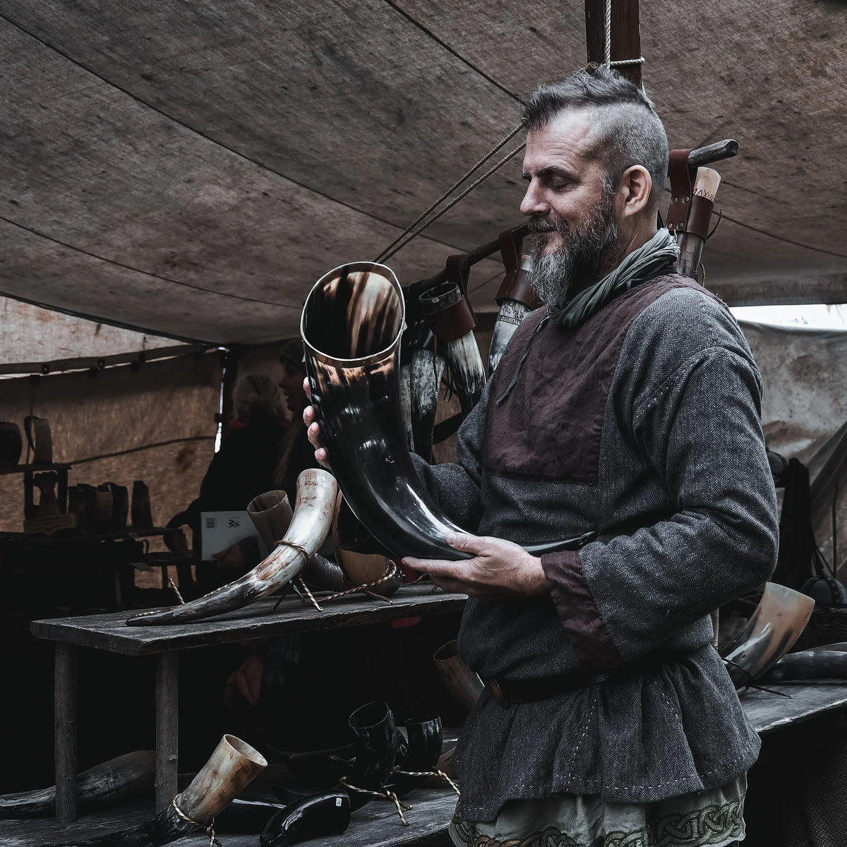 Stort dryckeshorn på cirka 4-5 liter hållet av vikingatida hantverkare i verkstad. Mässingsband vid öppningen, naturlig mörkbrun hornfärg, autentisk historisk miljö synlig i bakgrunden.