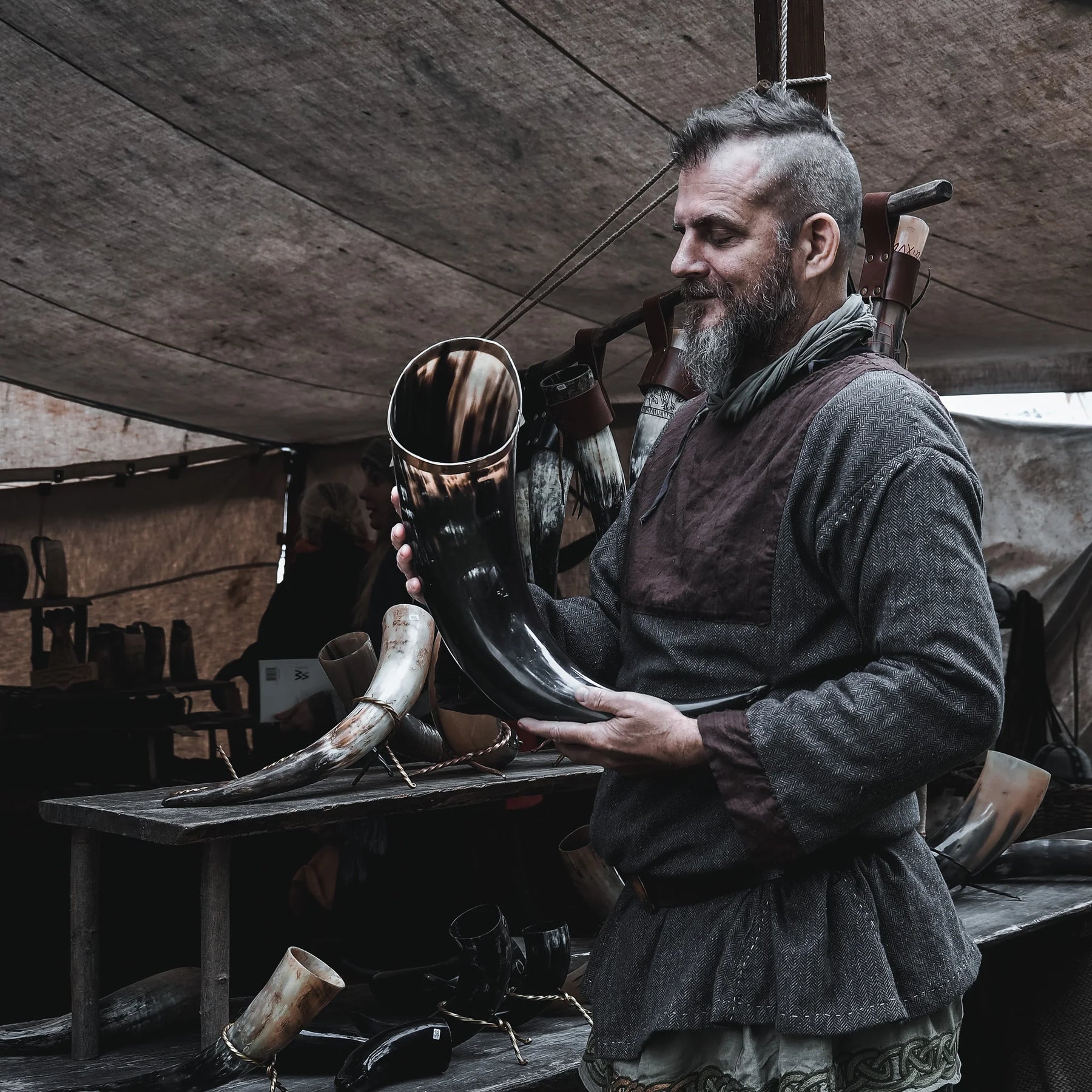 Stort dryckeshorn på cirka 4-5 liter hållet av vikingatida hantverkare i verkstad. Mässingsband vid öppningen, naturlig mörkbrun hornfärg, autentisk historisk miljö synlig i bakgrunden.