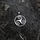 Triskele in circle – lying on dark bark, the chain visible above