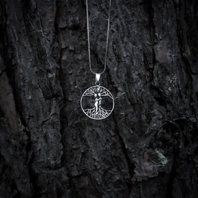 Silverkedja med cirkelformad amulett föreställande Yggdrasil, världsträdet, med synliga rötter och grenar på mörkrändig bakgrund.