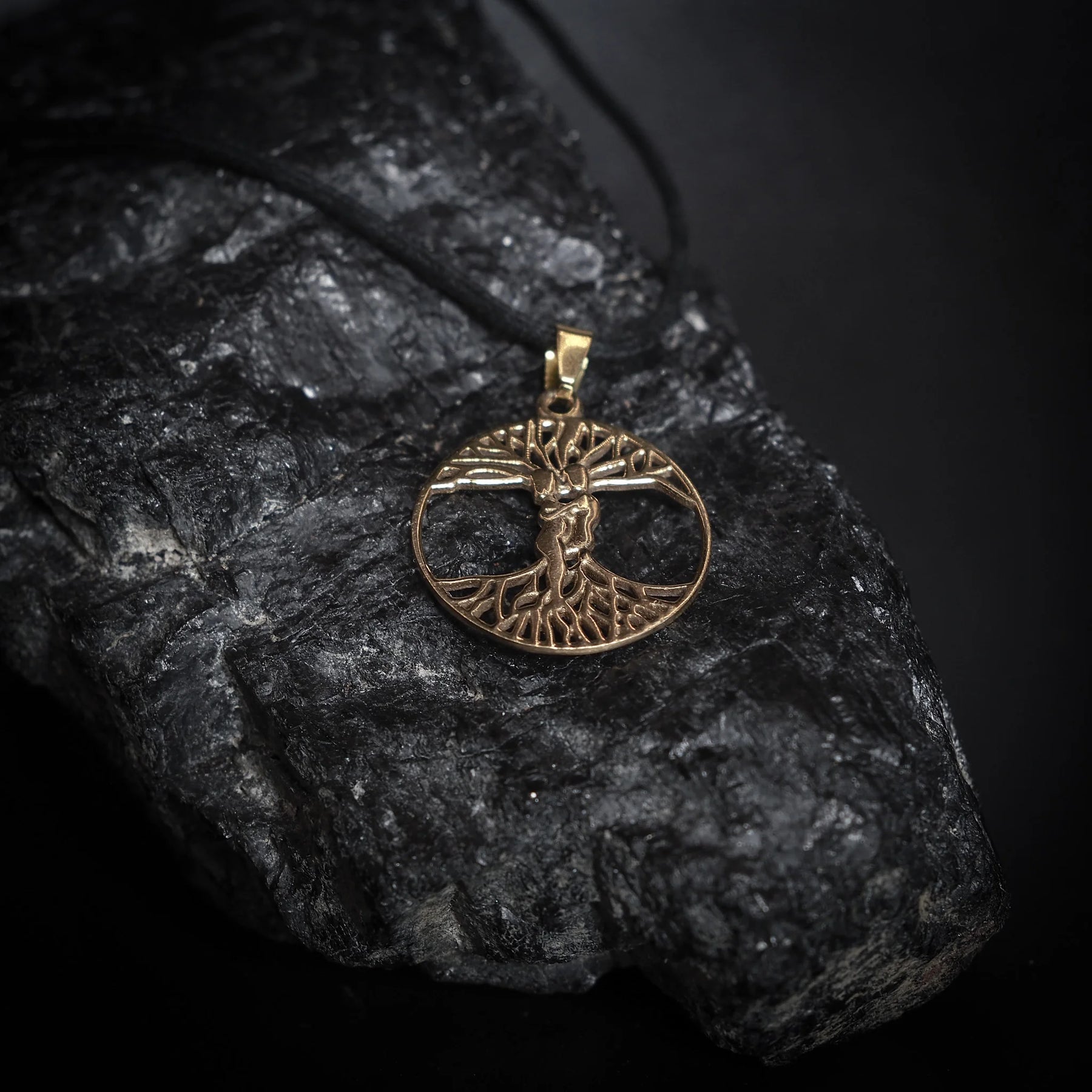 Ask och Embla-amulett i mässingsfärg med detaljerad Yggdrasil-träd design fotograferad på mörk sten