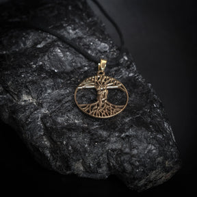 Ask och Embla-amulett i mässingsfärg med detaljerad Yggdrasil-träd design fotograferad på mörk sten