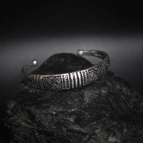 Närbild av silverpläterat mässingsarmband med detaljerade vikingegeometriska mönster på mörk stenstextur bakgrund