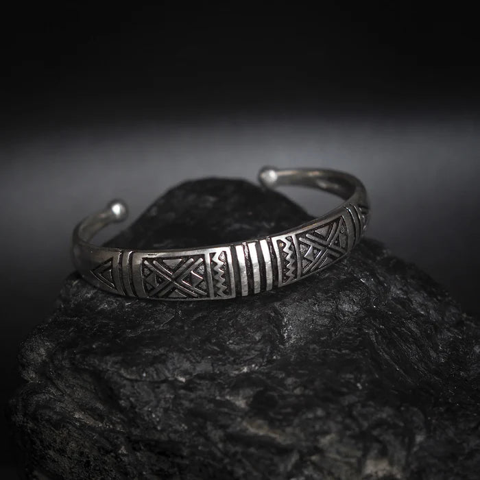 Närbild av silverpläterat mässingsarmband med detaljerade vikingegeometriska mönster på mörk stenstextur bakgrund