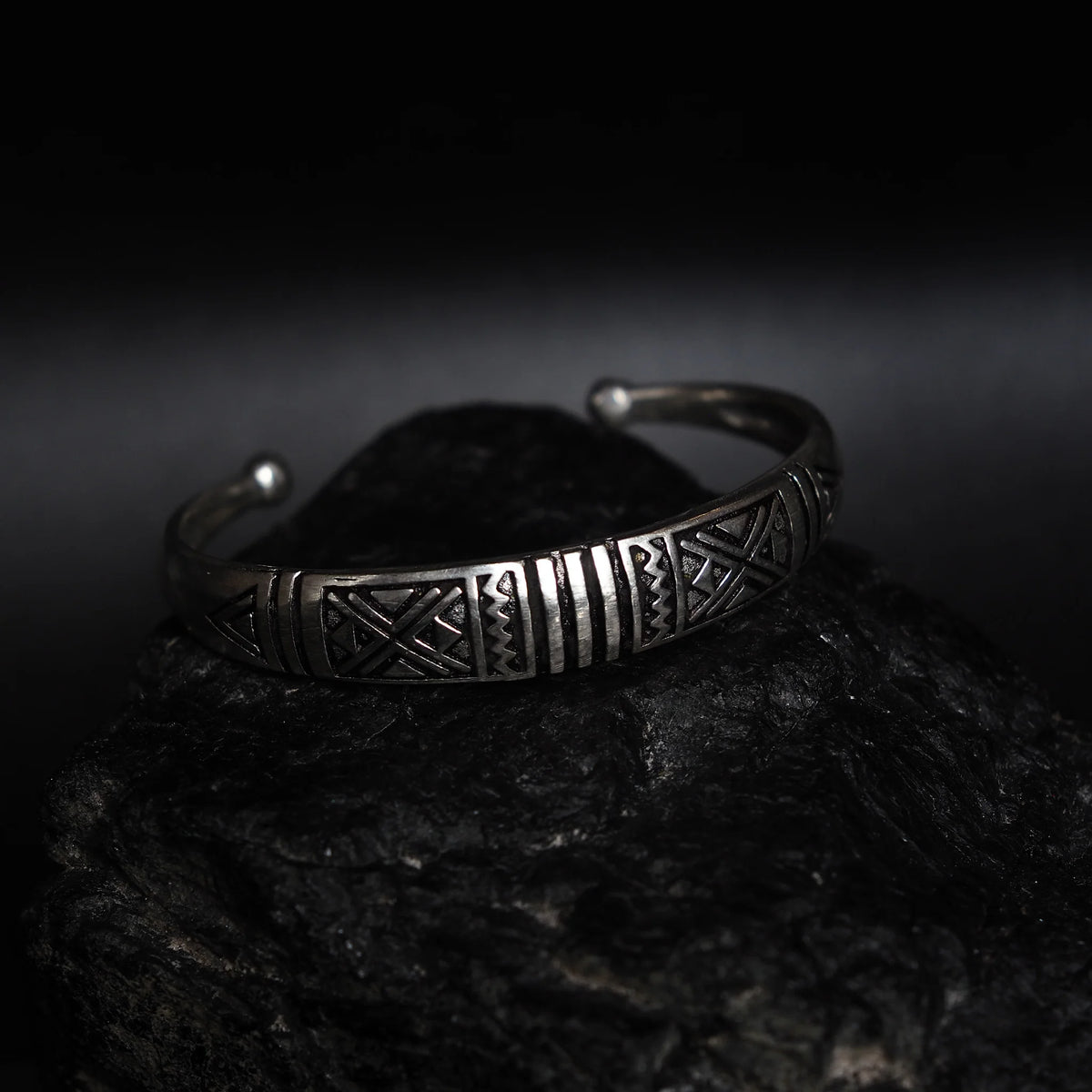 Välvt armband med dekor, silverpläterad, mot mörk bakgrund.