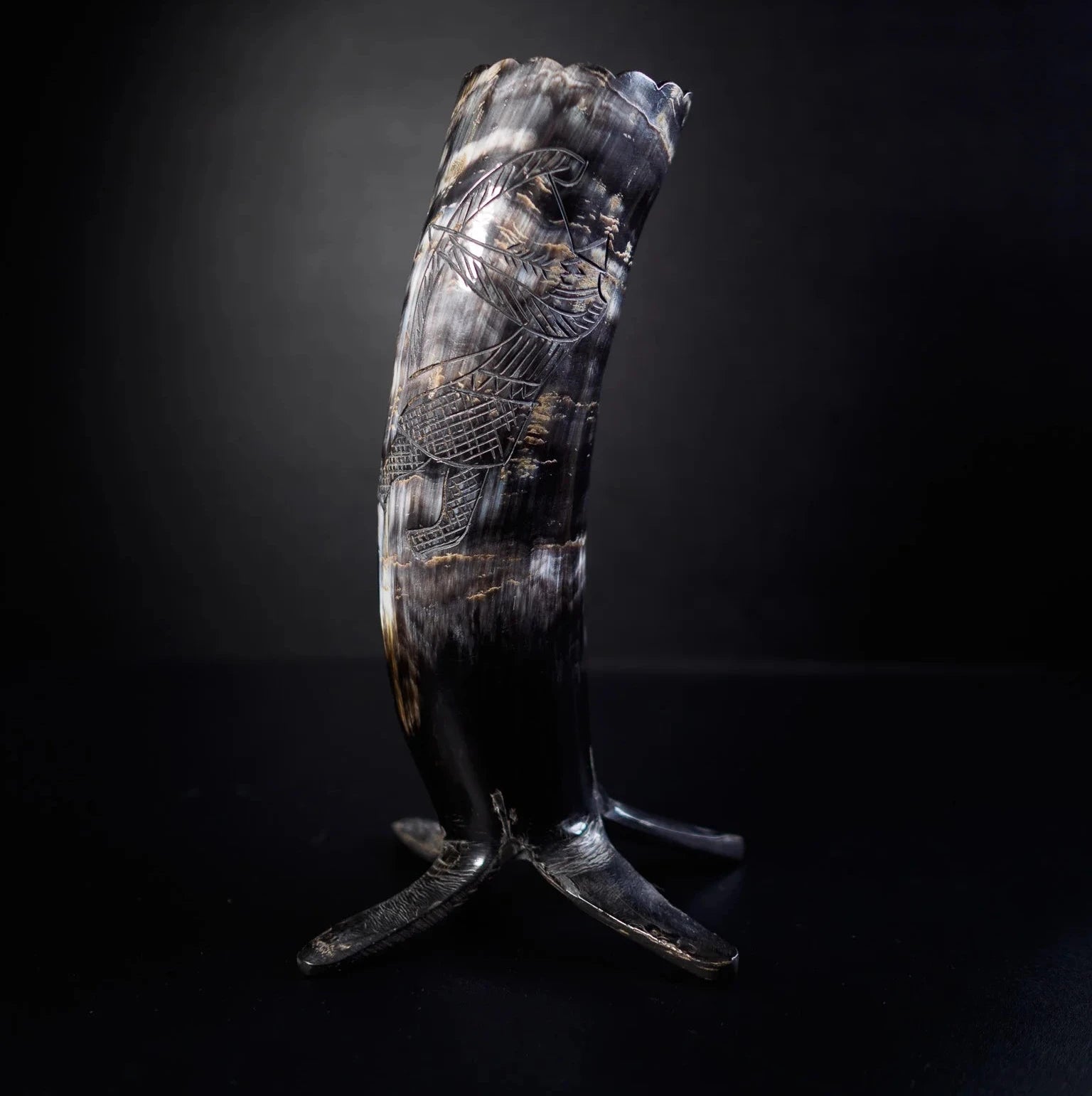 En organisk hornbägare på metallstativ med mörkbrunt och gräddigt patina. Gravering visar vikingaskepp från topp till botten med detaljerade sälmönster och gränsor med interlacing-designs.